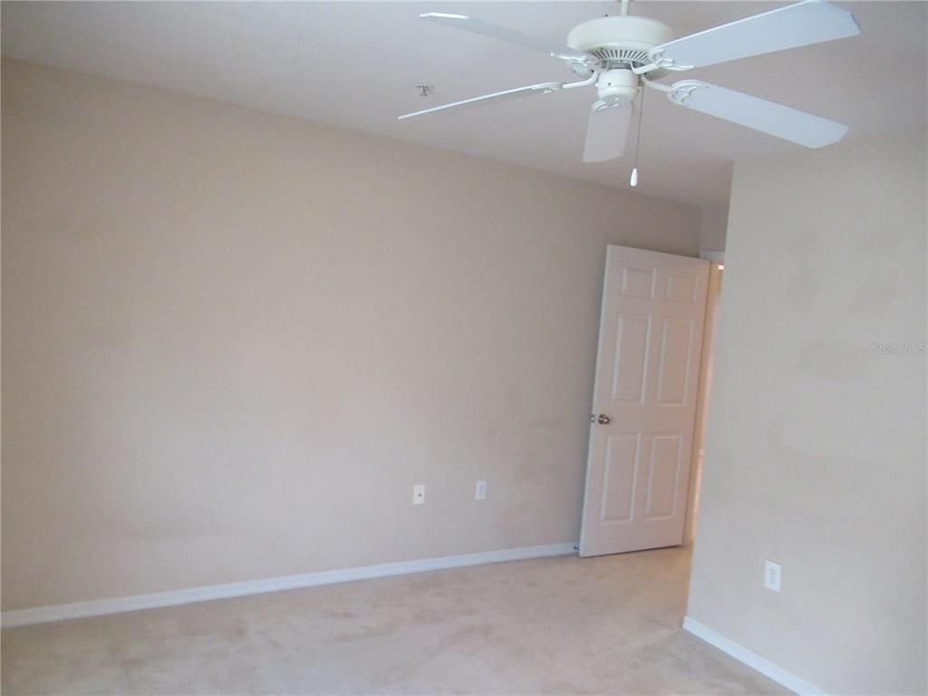 An empty bedroom with beige walls, tan carpeting, a white ceiling fan, and an open door — 5601 ROSEHILL ROAD UNIT 203, SARASOTA, FL