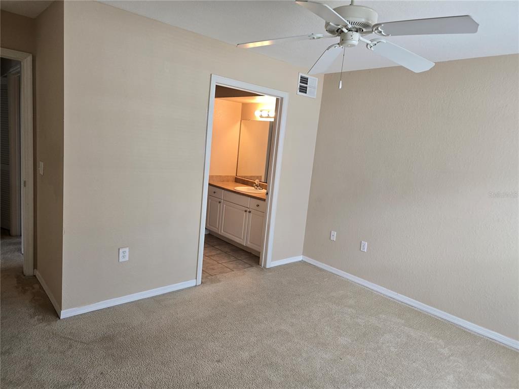 A carpeted bedroom features a ceiling fan and an open doorway leading to a bathroom — 5601 ROSEHILL ROAD UNIT 203, SARASOTA, FL