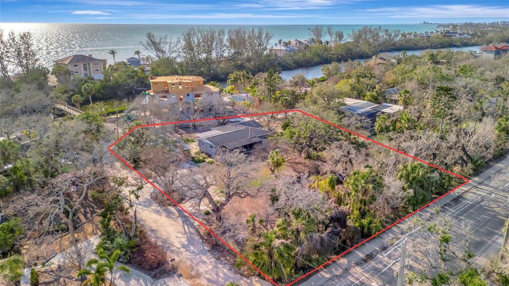 An aerial view shows a house on a large, wooded lot near a coastal waterway — 8555 HERON LAGOON CIRCLE, SARASOTA, FL