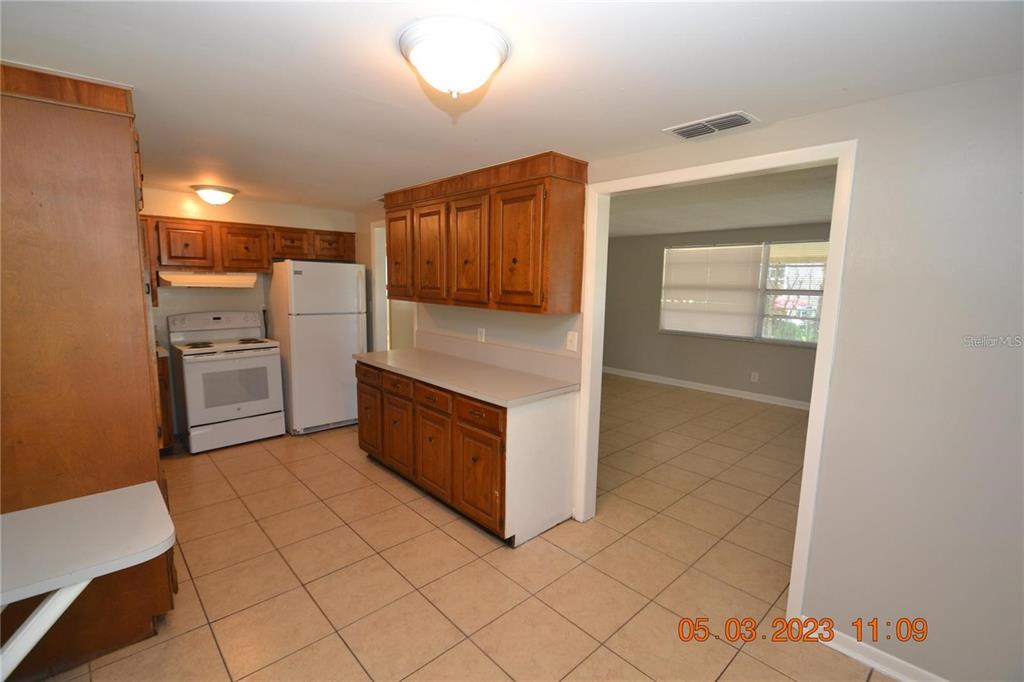 A kitchen with wood cabinets, white appliances, and tile flooring opens into a living area — 300 MIDWOOD DRIVE, PLANT CITY, FL