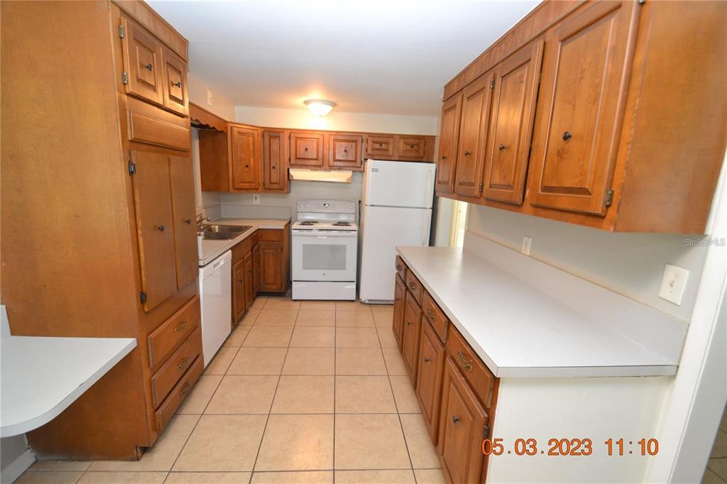 A kitchen features wood cabinets, white appliances, light countertops, and beige tile flooring — 300 MIDWOOD DRIVE, PLANT CITY, FL