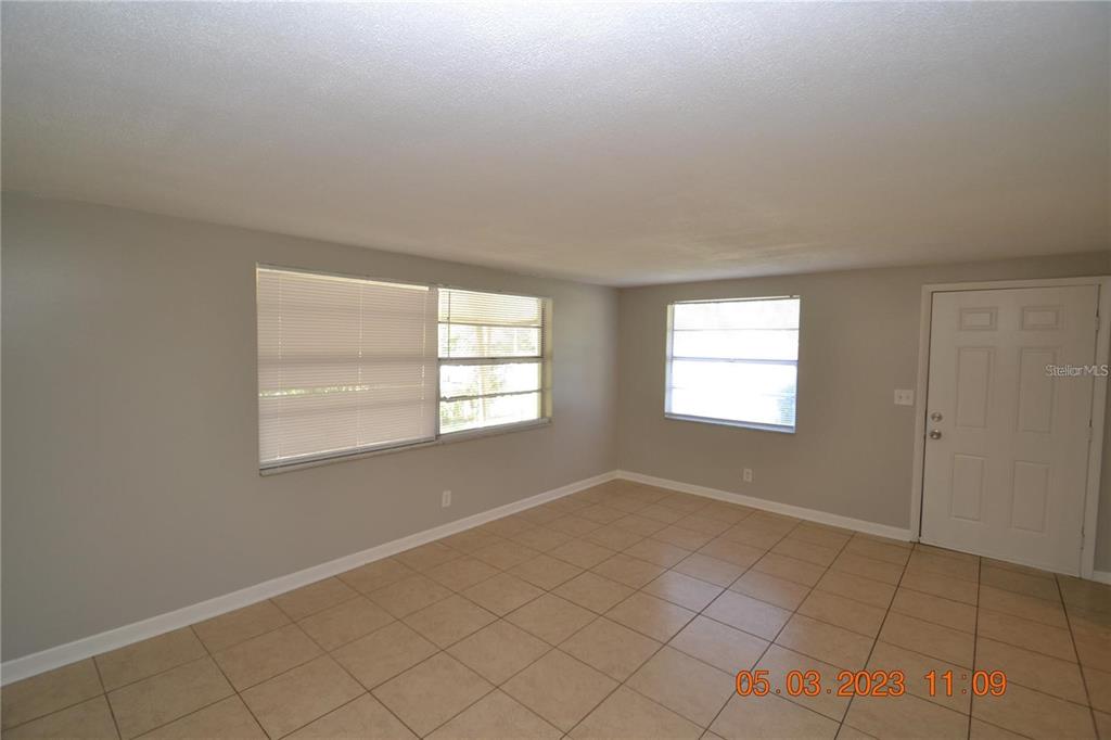 An empty room features light-colored walls, beige tile flooring, two windows, and a white door — 300 MIDWOOD DRIVE, PLANT CITY, FL