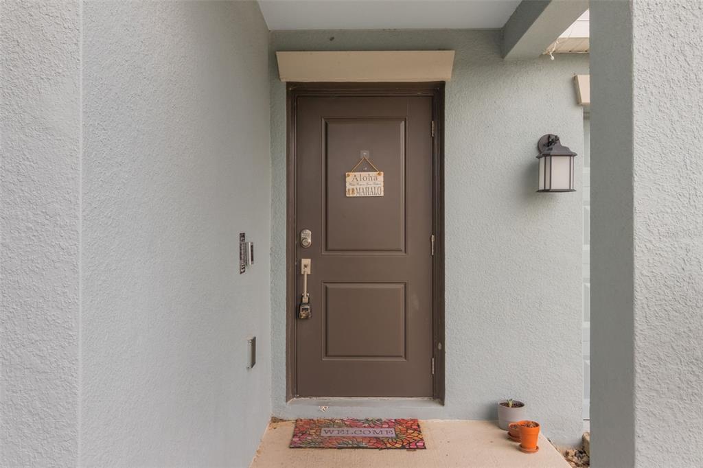 A brown front door with an Aloha sign sits under a covered entryway — 621 SILVER PALM DRIVE, HAINES CITY, FL