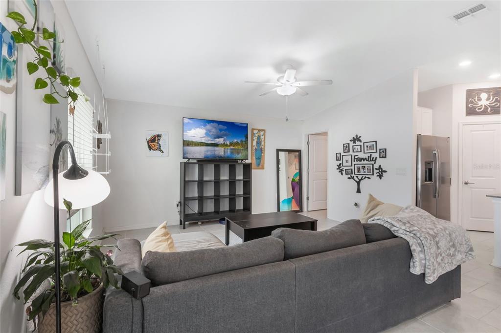 A living room features a grey sectional sofa, a television on a shelf, and tile flooring — 621 SILVER PALM DRIVE, HAINES CITY, FL