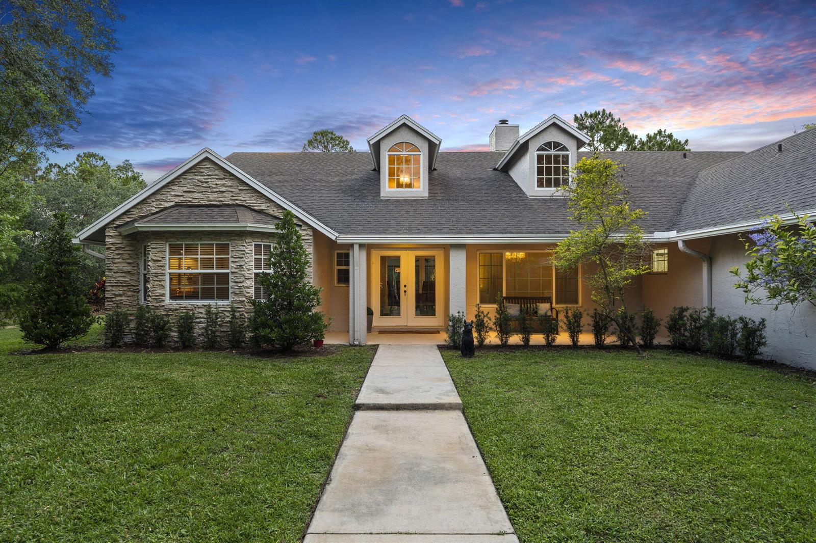 A single-story house with stone veneer, a concrete walkway, and two dormer windows at dusk — 17225 Mare Lane, Loxahatchee FL 33470, LOXAHATCHEE, FL