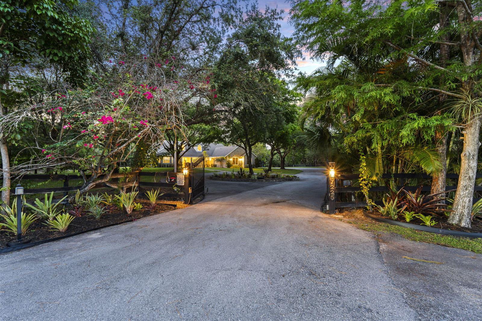 A paved driveway leads through an open gate toward a house surrounded by lush trees — 17225 Mare Lane, Loxahatchee FL 33470, LOXAHATCHEE, FL