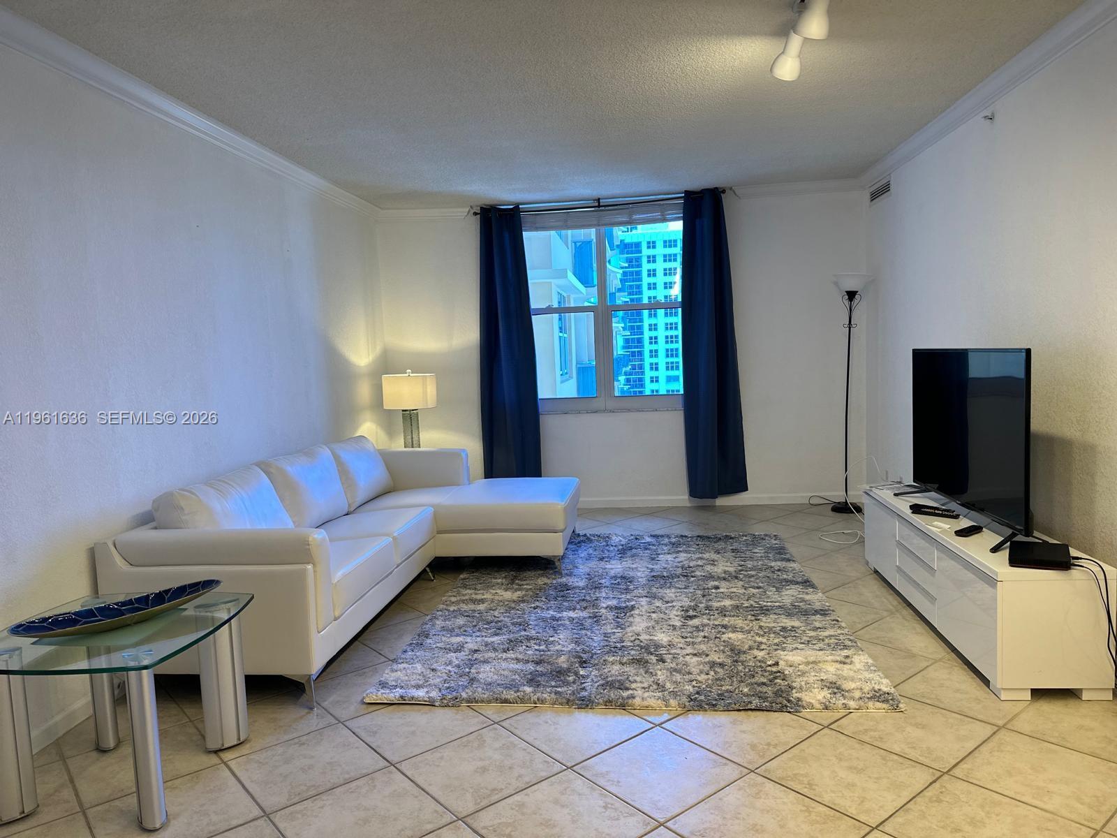 A living room features a white sectional sofa, a gray area rug, and a television console — 2501 S Ocean Dr # 1033, Hollywood FL 33019, HOLLYWOOD, FL