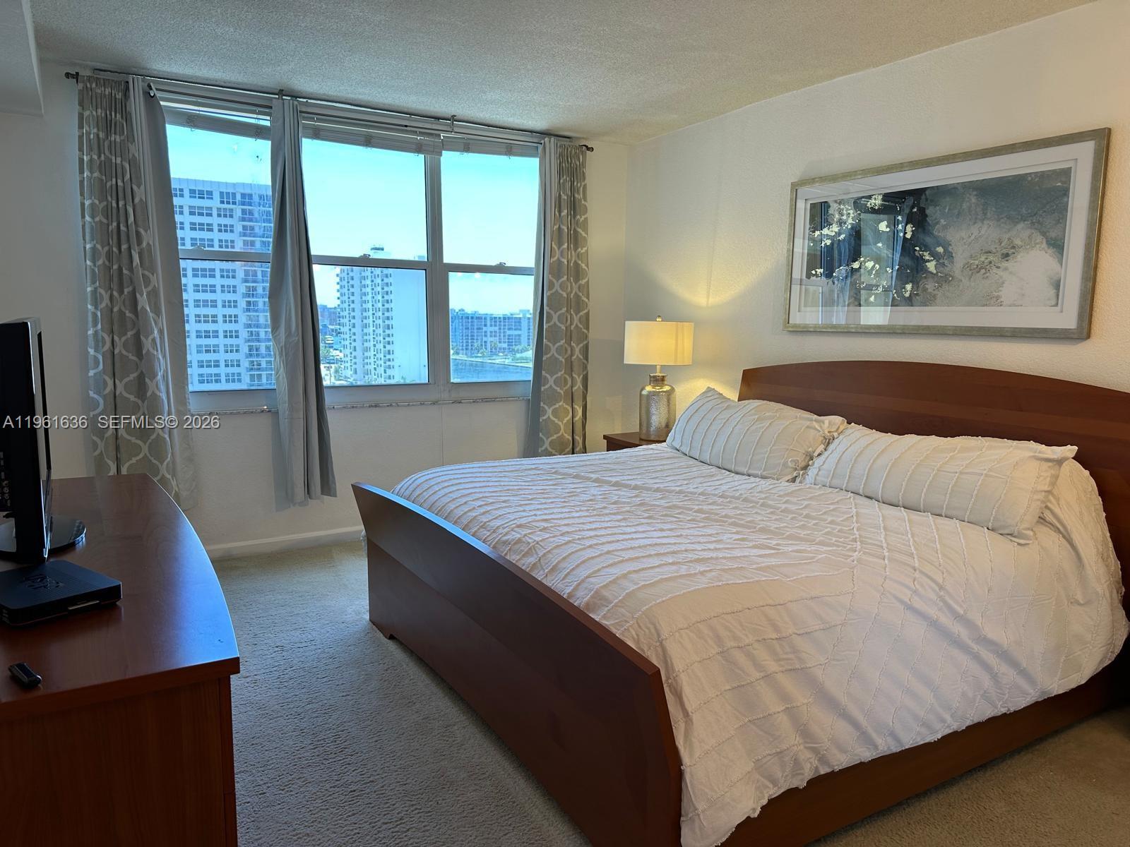 A bedroom features a wooden bed frame, a bedside lamp, and a large window view — 2501 S Ocean Dr # 1033, Hollywood FL 33019, HOLLYWOOD, FL