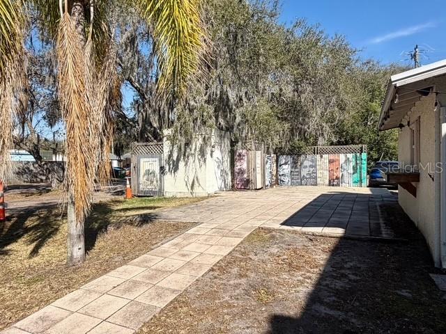 A paved walkway leads to a fenced area with decorative panels and mature trees — 417 & 419 SANFORD AVENUE, SANFORD, FL