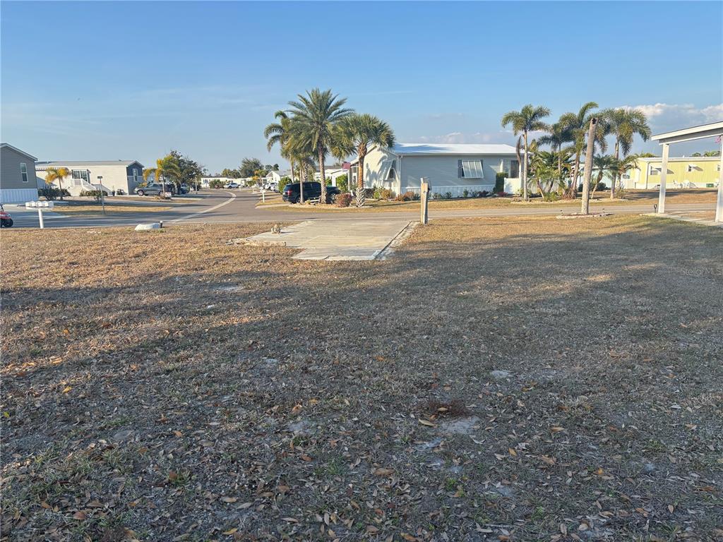 A vacant residential lot features a concrete pad with palm trees and neighboring mobile homes — 7437 LONGMONT LANE, PORT CHARLOTTE, FL
