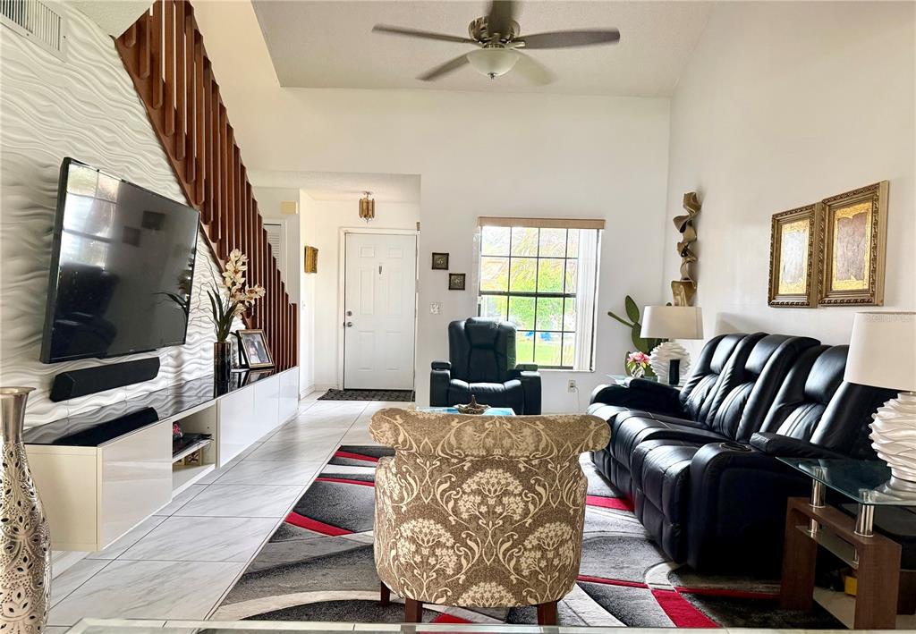 A living room features a black leather sofa, patterned armchair, tiled floors, and a staircase — 2139 BALBOA WAY, KISSIMMEE, FL