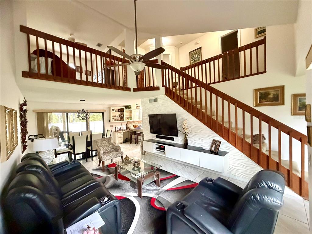 A living room features a vaulted ceiling, a staircase with wooden railings, and leather furniture — 2139 BALBOA WAY, KISSIMMEE, FL