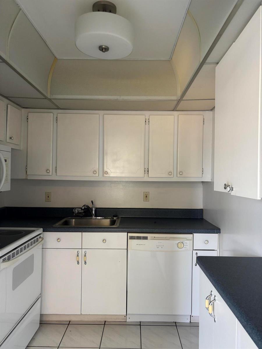 A kitchen features white cabinets, a dark countertop, a stainless steel sink, and tile flooring — 75 Sheffield D, West Palm Beach FL 33417, WEST PALM BEACH, FL