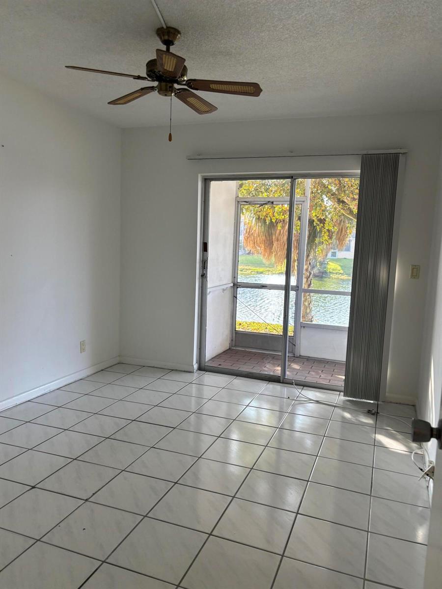 An empty room with white tile floors, a ceiling fan, and a sliding glass door — 75 Sheffield D, West Palm Beach FL 33417, WEST PALM BEACH, FL
