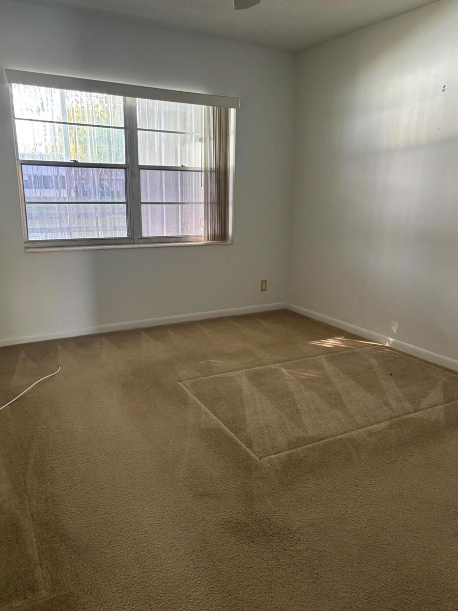 An empty bedroom features beige wall-to-wall carpeting, white walls, and a large window — 75 Sheffield D, West Palm Beach FL 33417, WEST PALM BEACH, FL