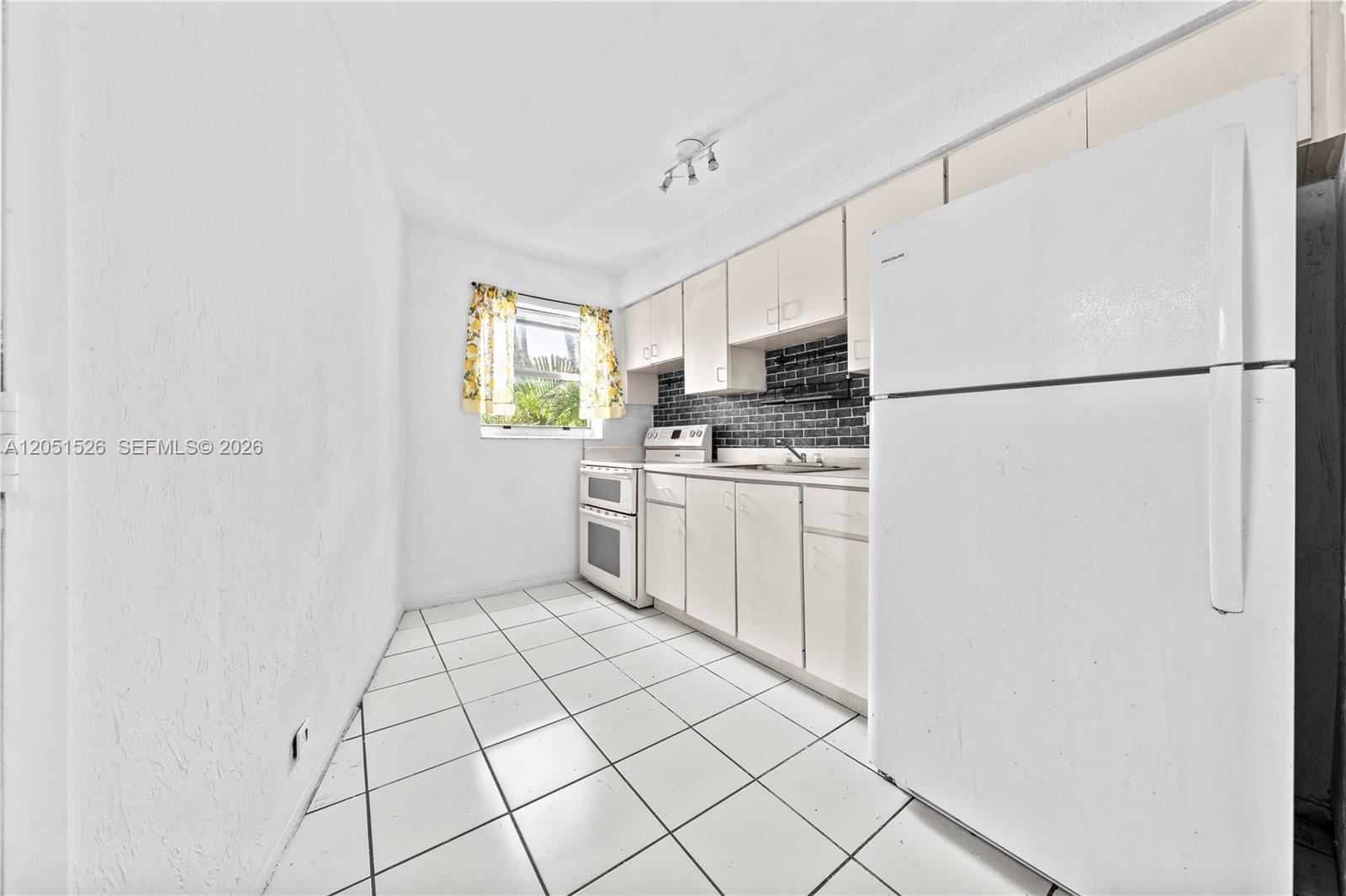 A kitchen features white cabinets, a black tiled backsplash, white appliances, and white floor tiles — 1610 NW N River Dr # 201, Miami FL 33125, MIAMI, FL