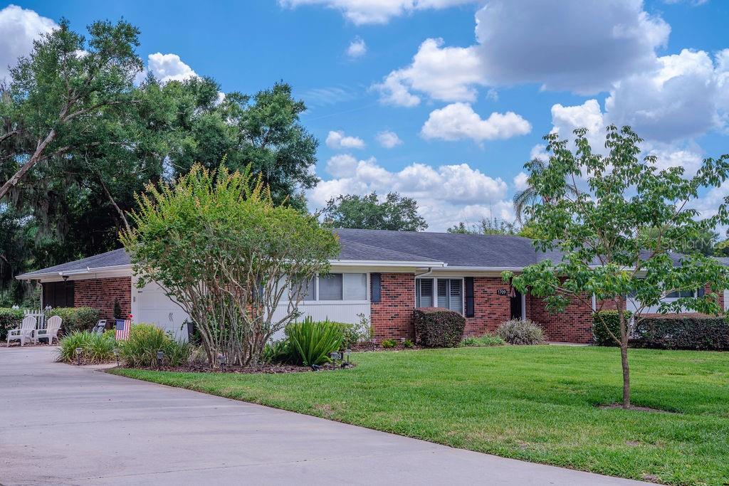 A single-story brick house with a concrete driveway, lawn, and trees under a cloudy sky — 1709 VIRGINIA COURT, LAKELAND, FL