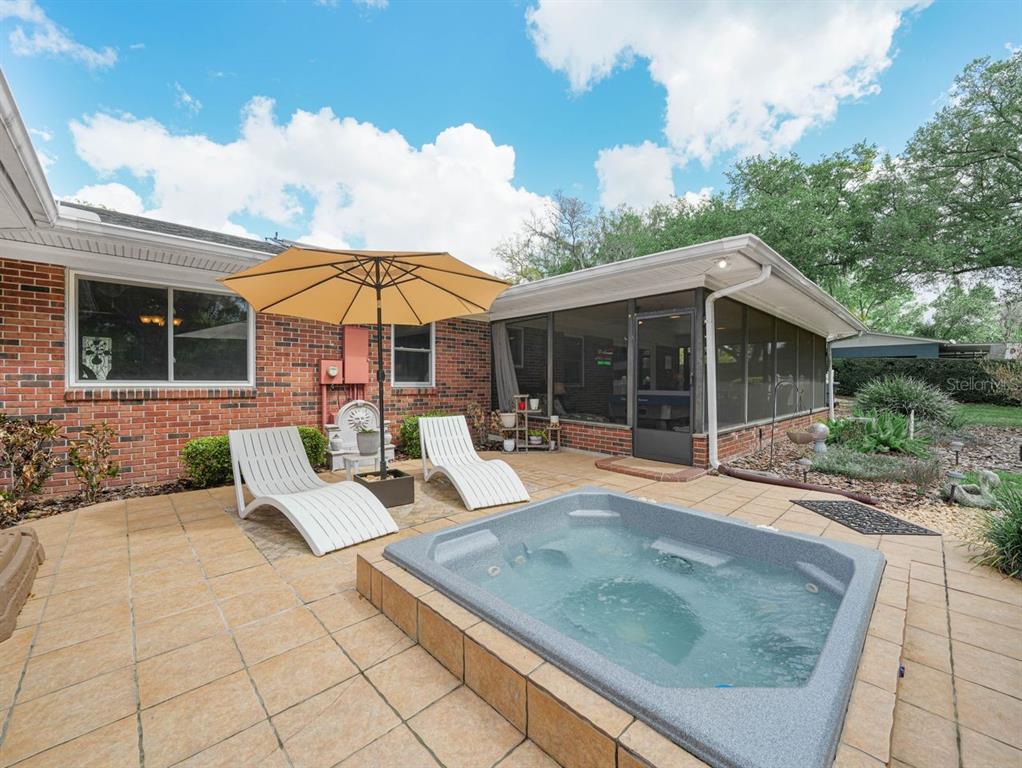 A brick house exterior features a patio with a hot tub, lounge chairs, and umbrella — 1709 VIRGINIA COURT, LAKELAND, FL