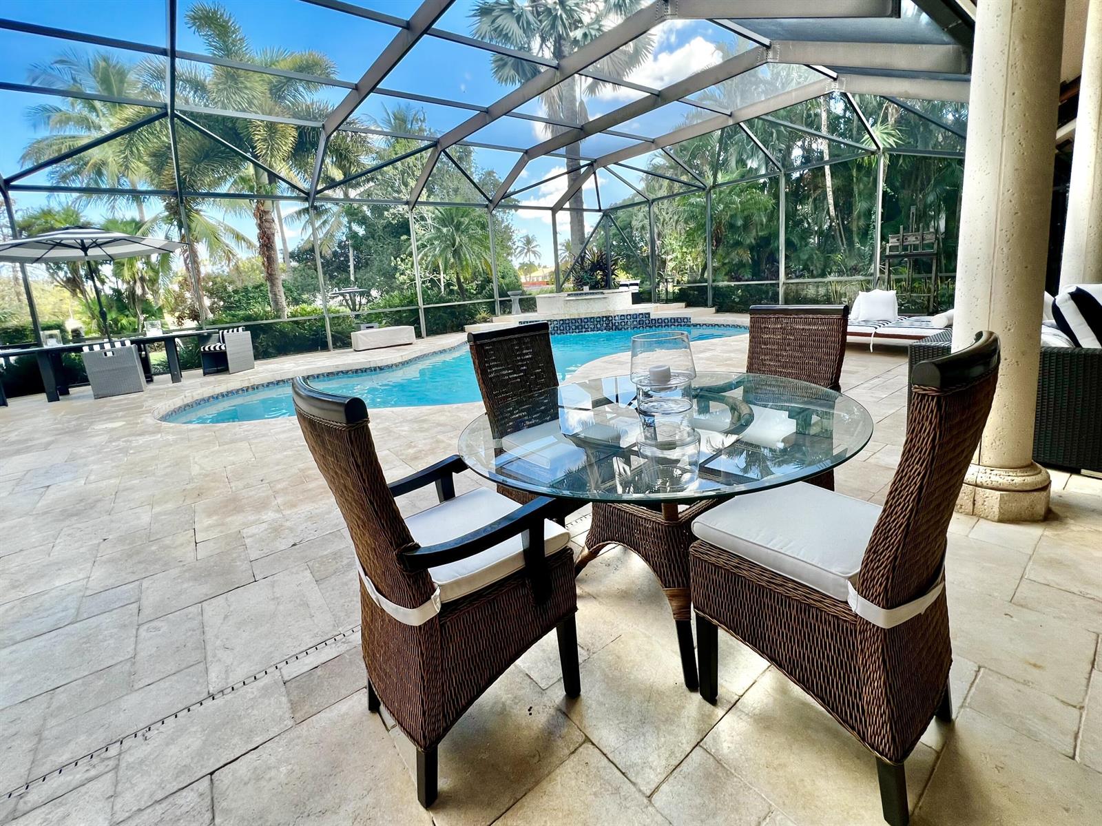 A glass-topped dining set sits on a stone patio inside a screened-in pool enclosure — 2050 Windsock Way, Wellington FL 33414, WELLINGTON, FL