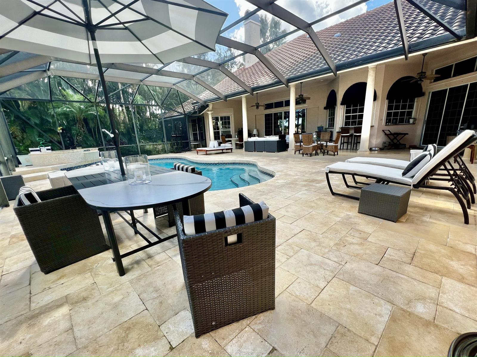 A covered patio features a swimming pool, outdoor dining set, and lounge chairs on stone pavers — 2050 Windsock Way, Wellington FL 33414, WELLINGTON, FL