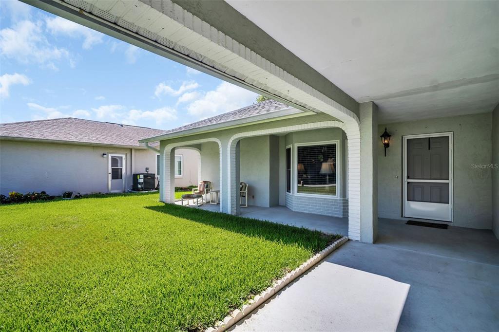 A covered patio with arched brick supports overlooks a green lawn and a neighboring house — 3960 TARPON POINTE CIRCLE, PALM HARBOR, FL