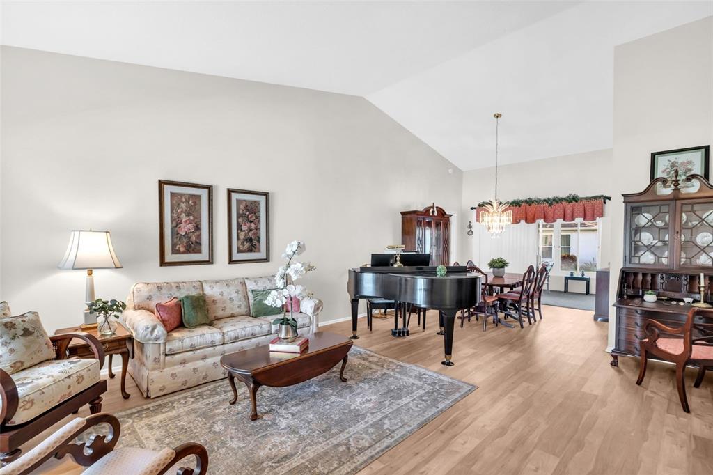 A living room with a grand piano, floral sofa, and light wood flooring — 3960 TARPON POINTE CIRCLE, PALM HARBOR, FL