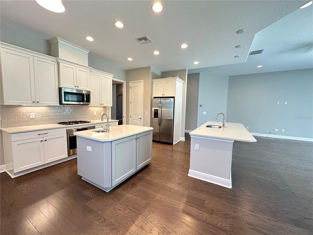 A kitchen features white cabinetry, quartz countertops, two islands, and dark hardwood flooring — 981 BEE BRANCH COURT, PALM HARBOR, FL