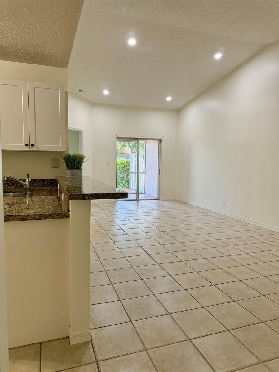A kitchen with granite countertops overlooks a tiled living area with a sliding glass door — 11289 SW 18th Court, Miramar FL 33025, MIRAMAR, FL
