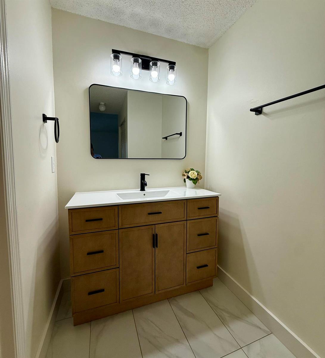 A bathroom features a wood vanity with a white countertop, black fixtures, and a rectangular mirror — 11289 SW 18th Court, Miramar FL 33025, MIRAMAR, FL