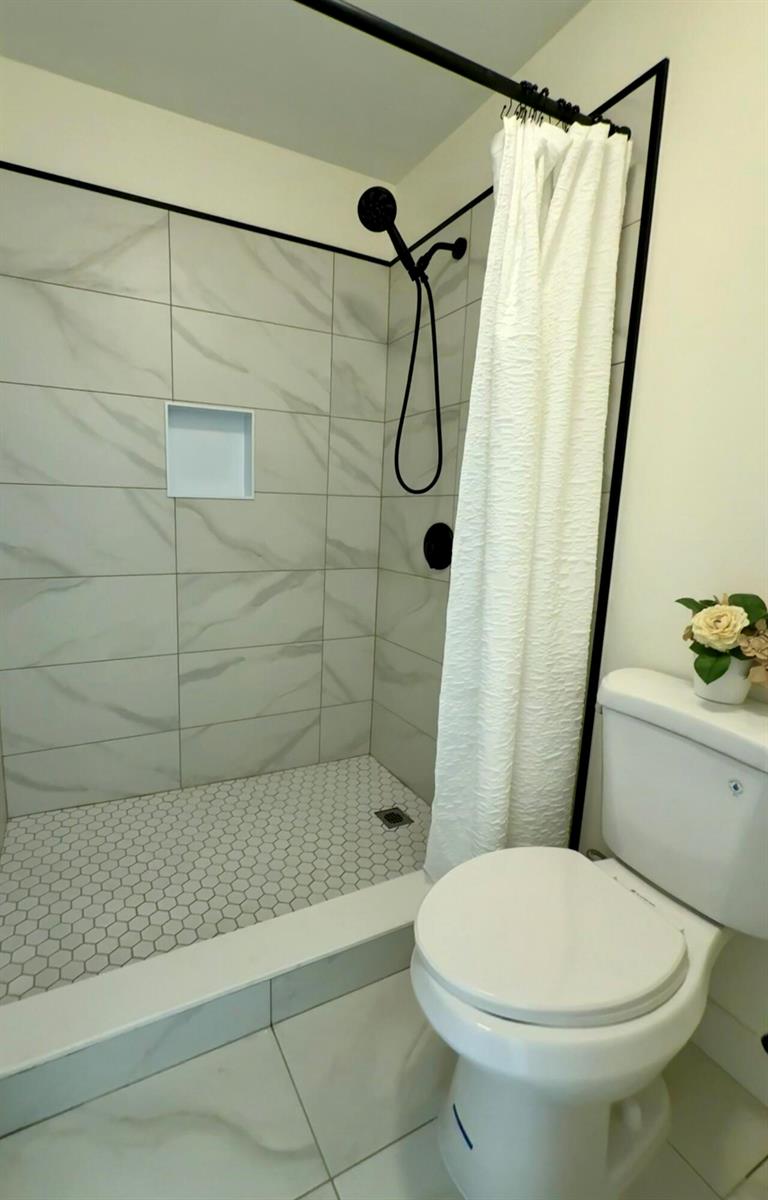 A bathroom features a walk-in shower with white marble-look tiles, black fixtures, and a toilet — 11289 SW 18th Court, Miramar FL 33025, MIRAMAR, FL