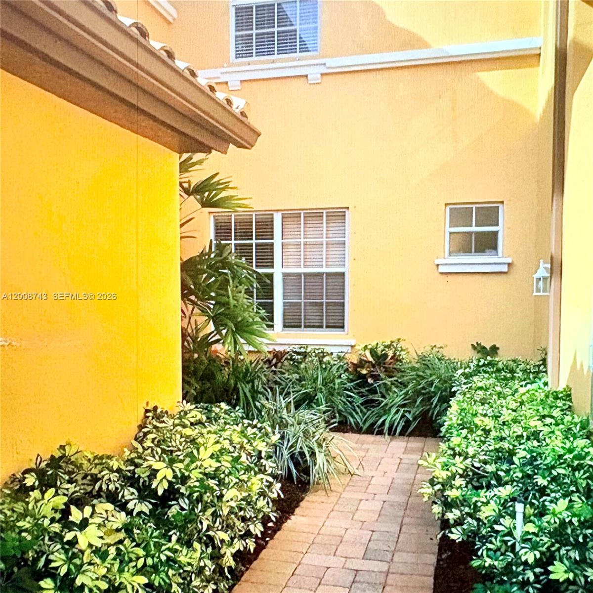 A paved walkway leads to a yellow stucco house with two windows and landscaping — 7993 NW 128th Ln # B, Parkland FL 33076, PARKLAND, FL