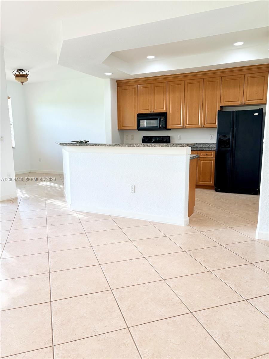 A kitchen features light wood cabinets, black appliances, a granite breakfast bar, and tile flooring — 7993 NW 128th Ln # B, Parkland FL 33076, PARKLAND, FL