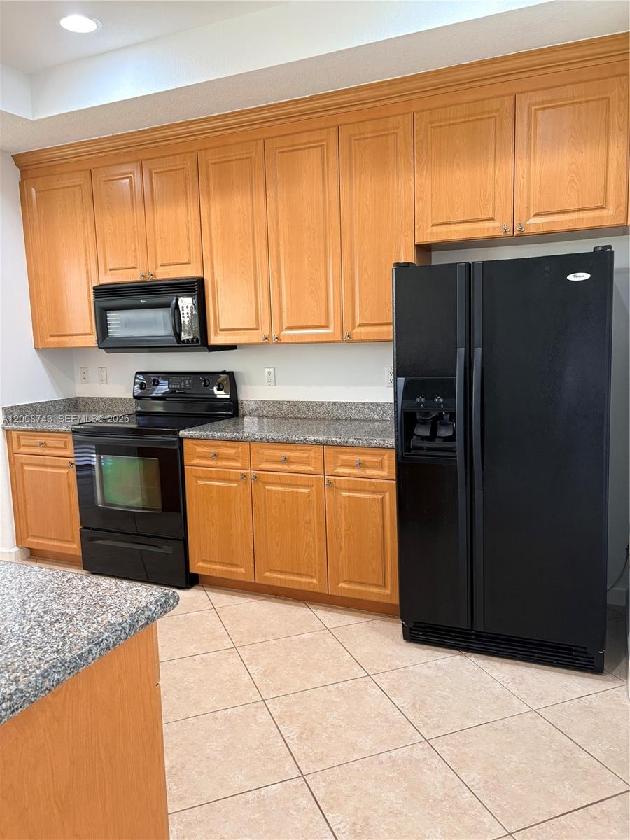 A kitchen features light wood cabinets, black appliances, and speckled granite countertops — 7993 NW 128th Ln # B, Parkland FL 33076, PARKLAND, FL