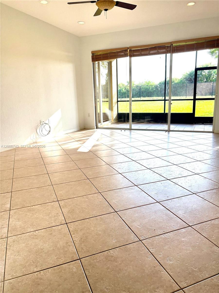 An empty room features light-colored tile flooring, a ceiling fan, and sliding glass doors — 7993 NW 128th Ln # B, Parkland FL 33076, PARKLAND, FL