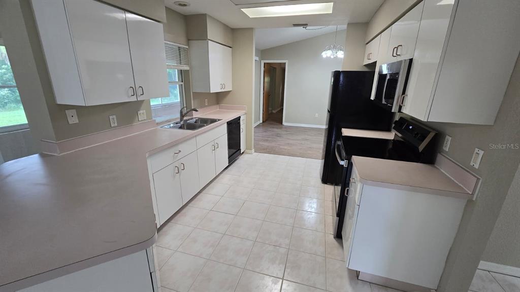 A kitchen features white cabinets, light-colored countertops, tile flooring, and black appliances — 469 DORCHESTER STREET, PORT CHARLOTTE, FL