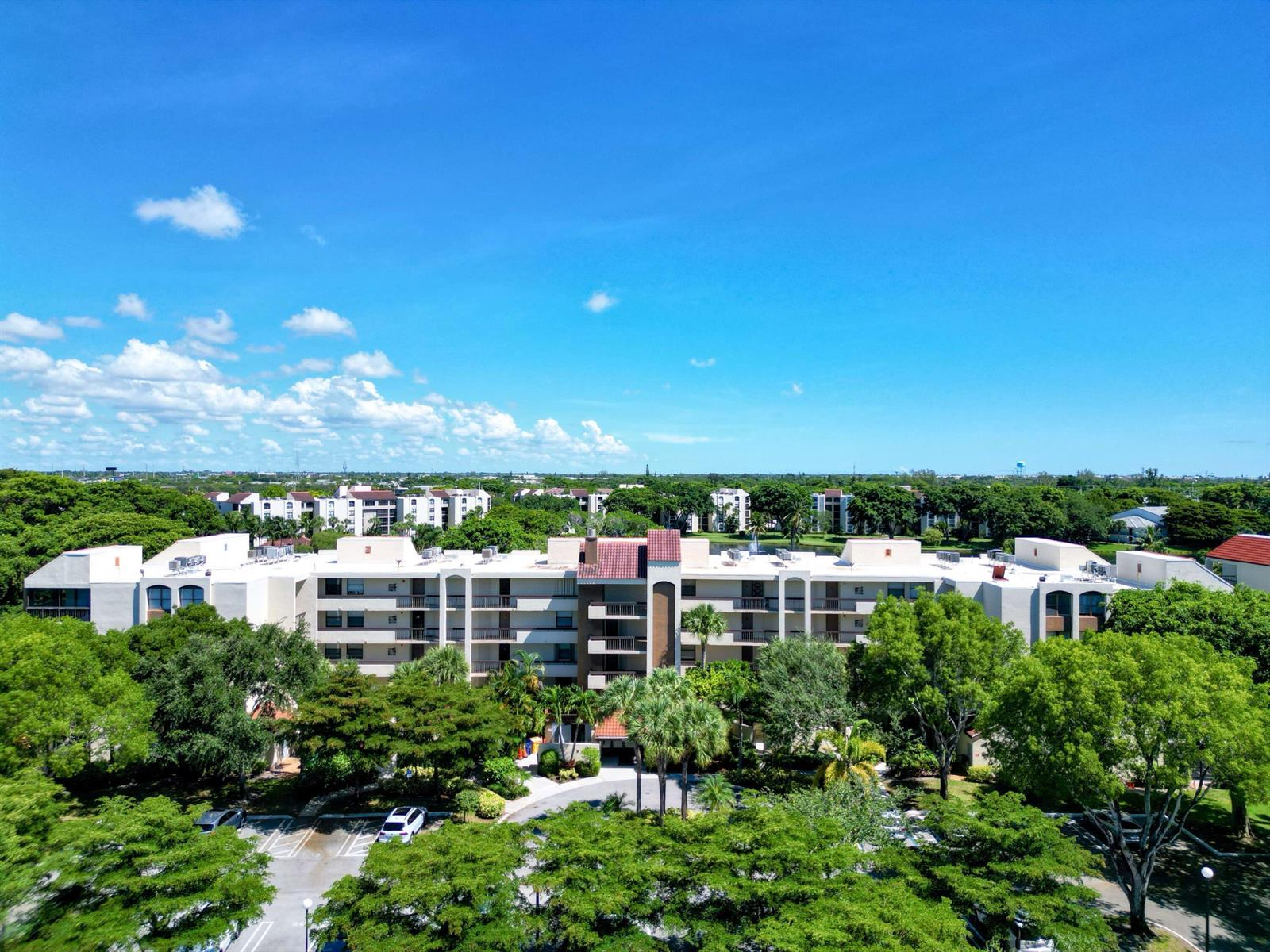 An aerial view of a multi-story apartment complex surrounded by trees and a parking lot — 955 Egret Circle # 102, Delray Beach FL 33444, DELRAY BEACH, FL