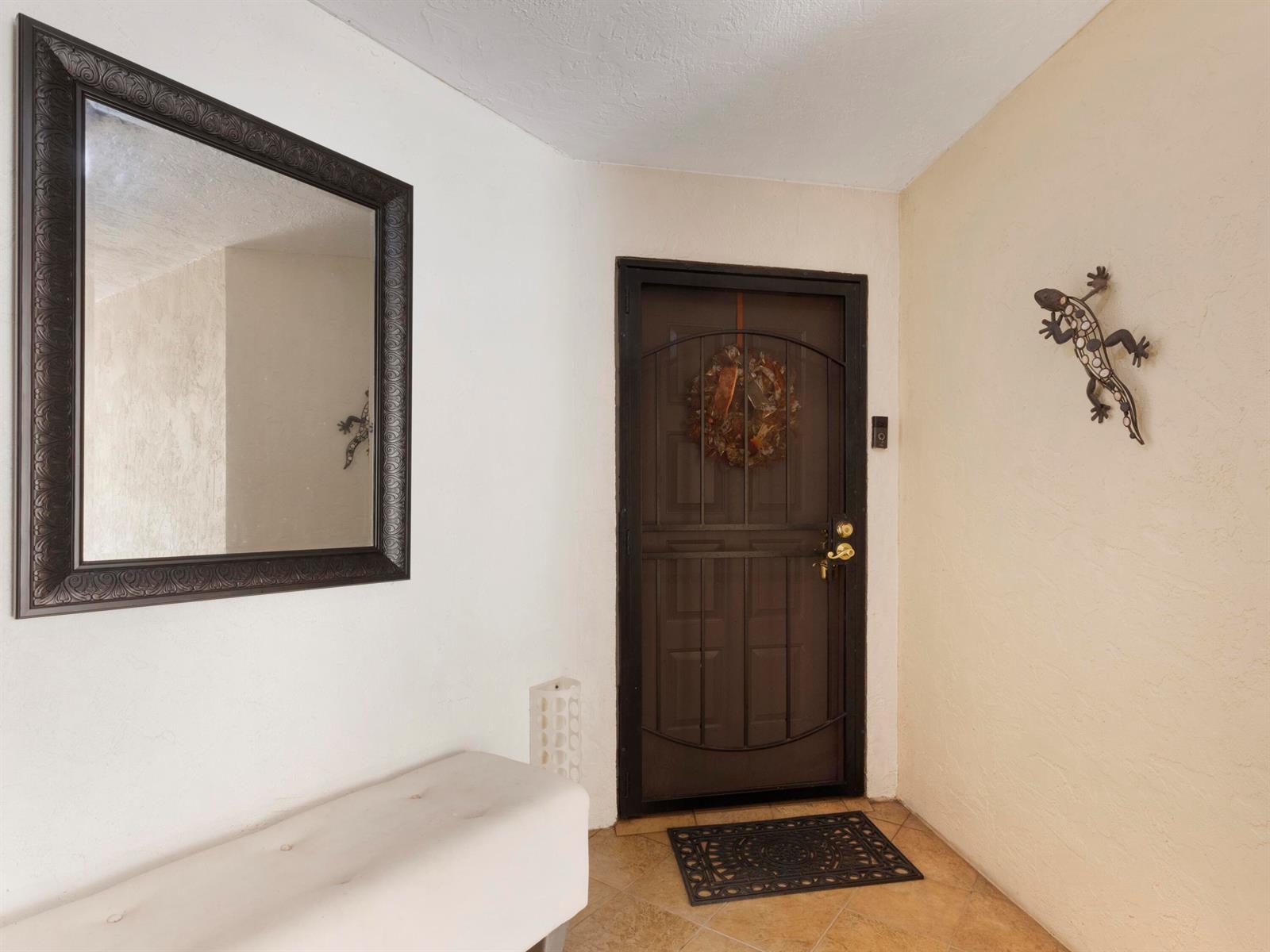 An entryway features a dark-framed mirror, a bench, a security door, and a lizard wall decoration — 955 Egret Circle # 102, Delray Beach FL 33444, DELRAY BEACH, FL