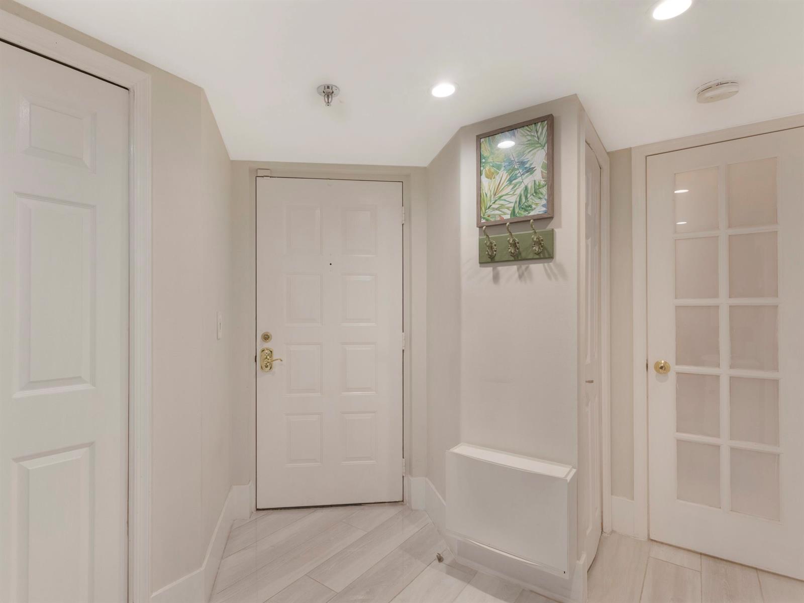 A bright entryway features light wood-look flooring, a white front door, and a wall-mounted coat rack — 955 Egret Circle # 102, Delray Beach FL 33444, DELRAY BEACH, FL