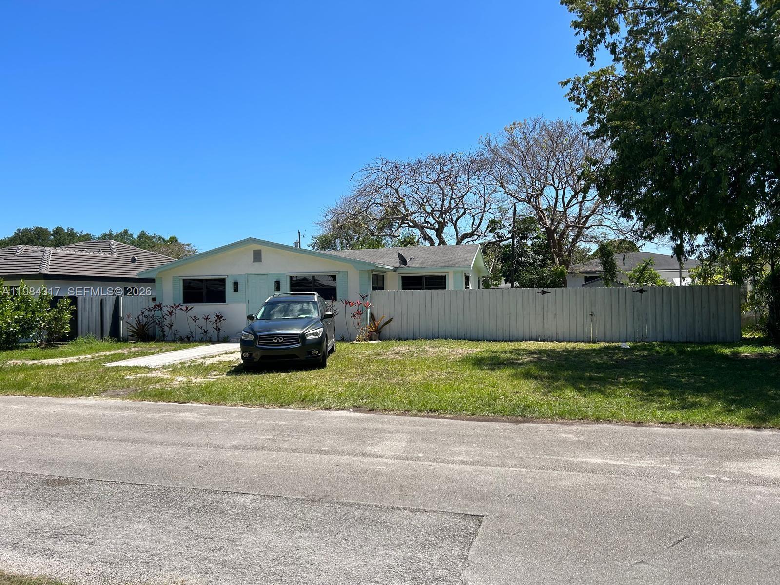 A single-story house with a light-colored exterior and a white fence sits behind a car — 8866 SW 126th St, Miami FL 33176, MIAMI, FL