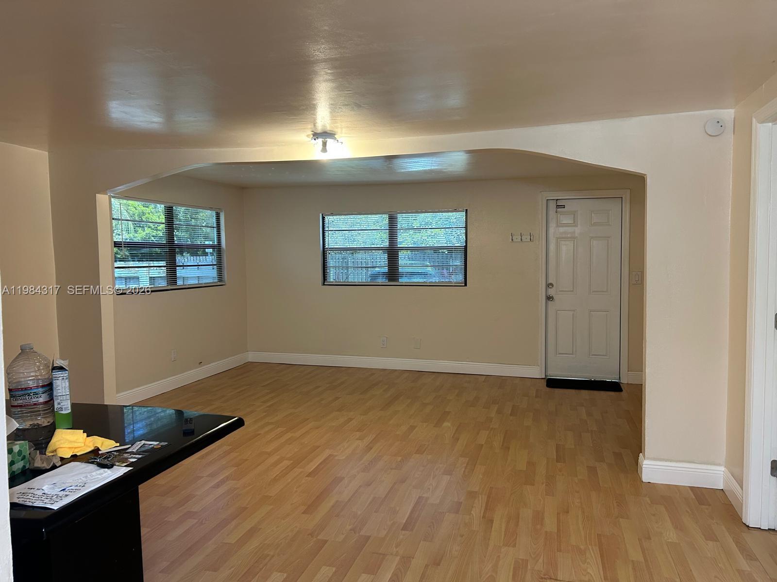 An empty living room features light wood flooring, beige walls, and a white entry door — 8866 SW 126th St, Miami FL 33176, MIAMI, FL