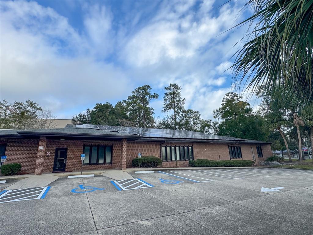 A brick commercial building features a solar panel array on its roof and a parking lot — 7510 NW 4TH BOULEVARD, GAINESVILLE, FL