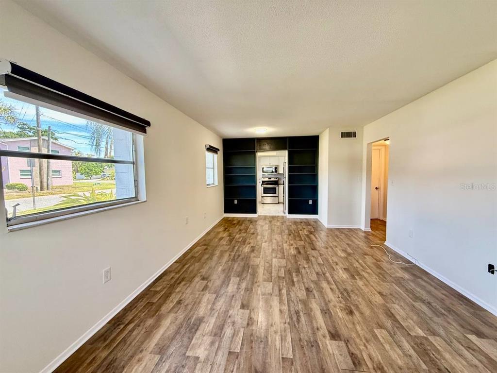 An empty living room features wood-look flooring, white walls, and a large black built-in shelving unit — 3460 32ND AVENUE N UNIT 101, ST PETERSBURG, FL