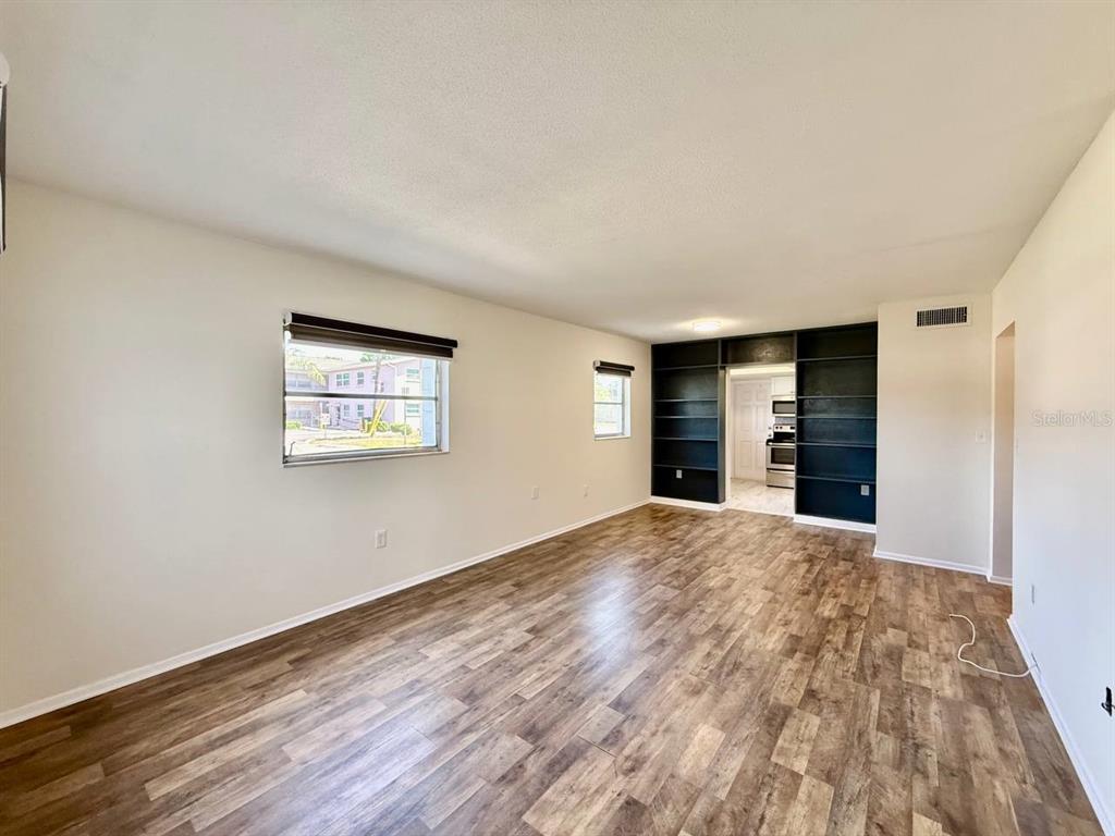 An empty living room features wood-look flooring, light walls, and black built-in shelving — 3460 32ND AVENUE N UNIT 101, ST PETERSBURG, FL