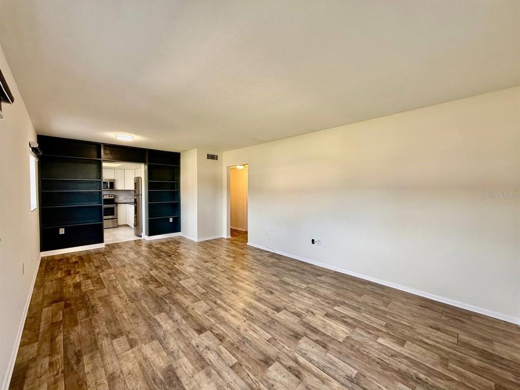A living room features wood-look flooring, white walls, and a large black built-in shelving unit — 3460 32ND AVENUE N UNIT 101, ST PETERSBURG, FL
