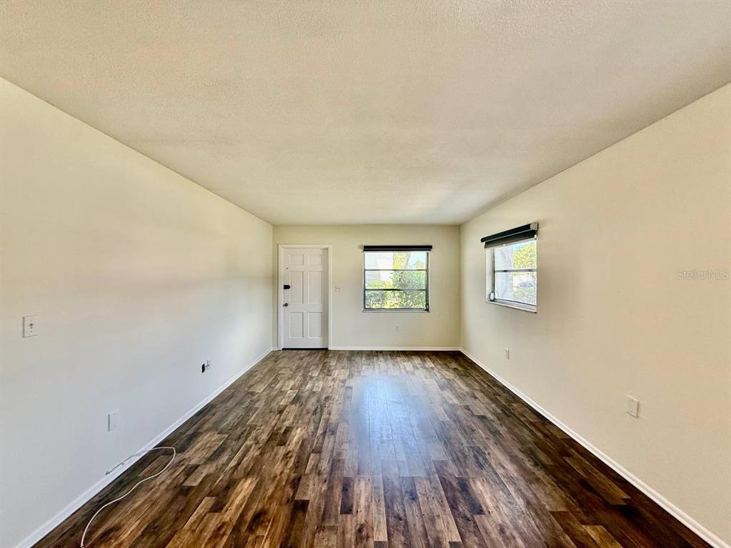 An empty living room features wood-look flooring, light-colored walls, and two windows — 3460 32ND AVENUE N UNIT 101, ST PETERSBURG, FL