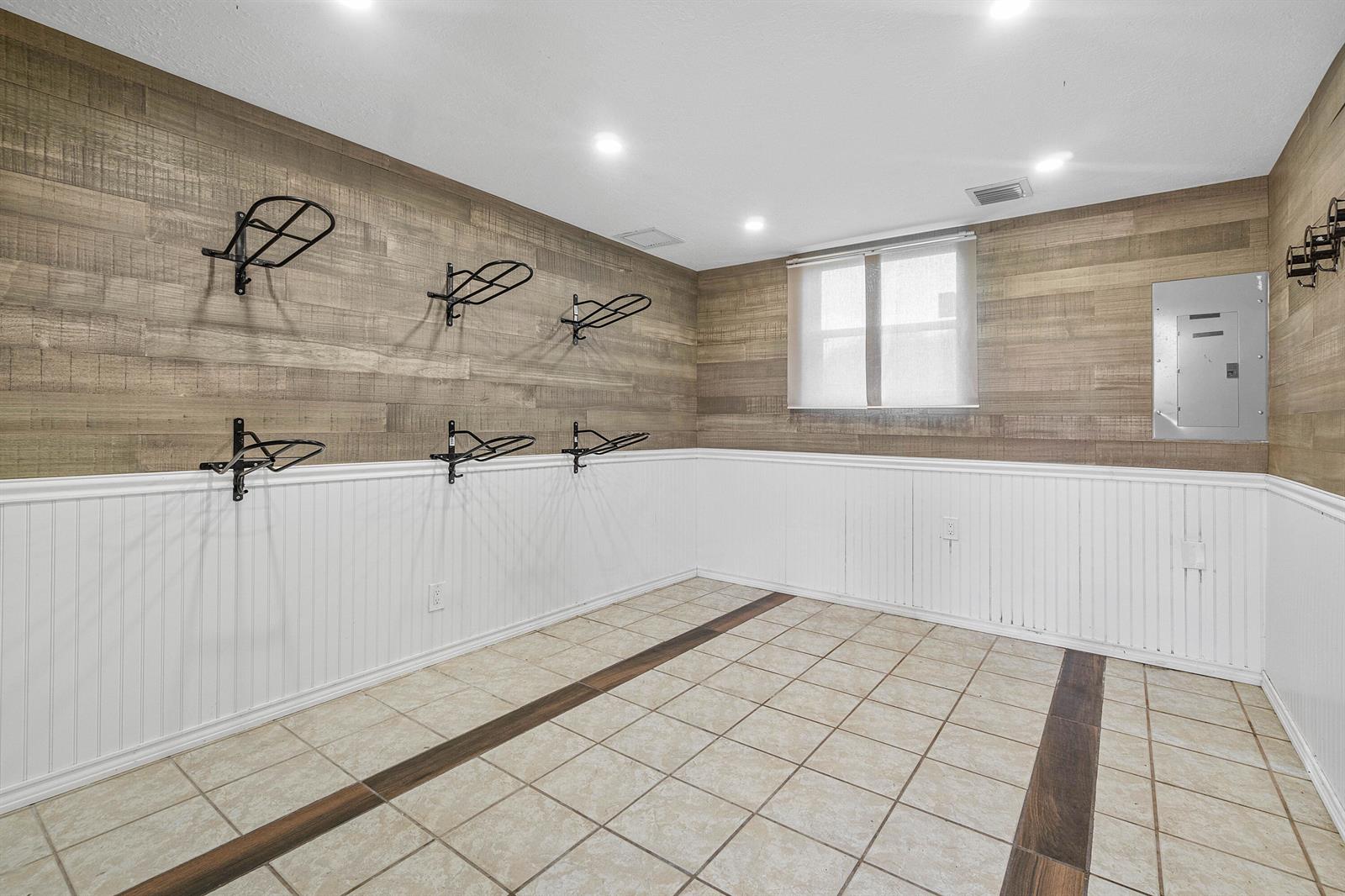 A room with wood-paneled walls, white wainscoting, tile flooring, and several wall-mounted metal racks — 2080 Canter Way, Wellington FL 33414, WELLINGTON, FL