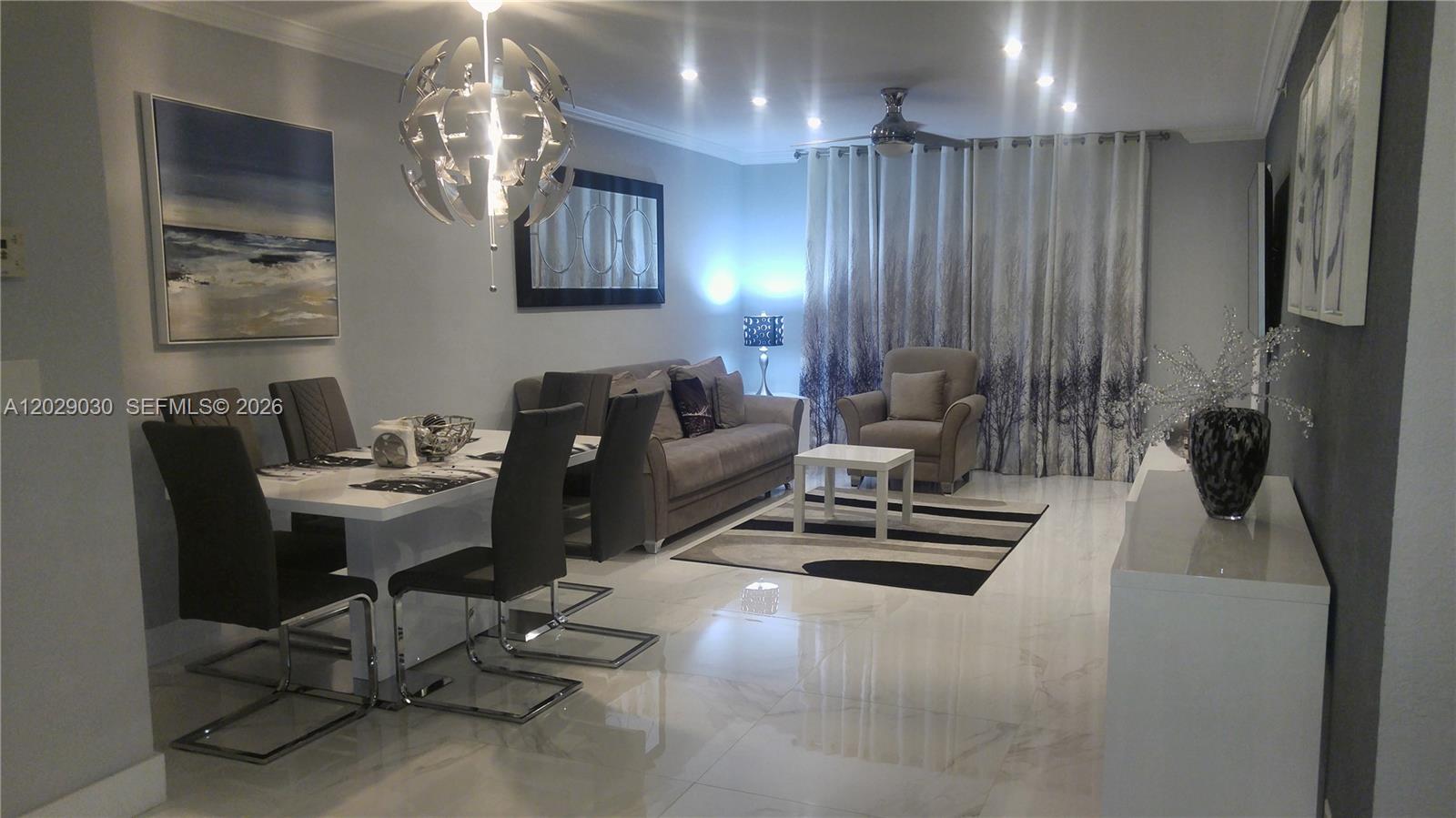 A modern living and dining room features white tile floors, gray furniture, and a chandelier — 2501 S Ocean Dr # L04, Hollywood FL 33019, HOLLYWOOD, FL