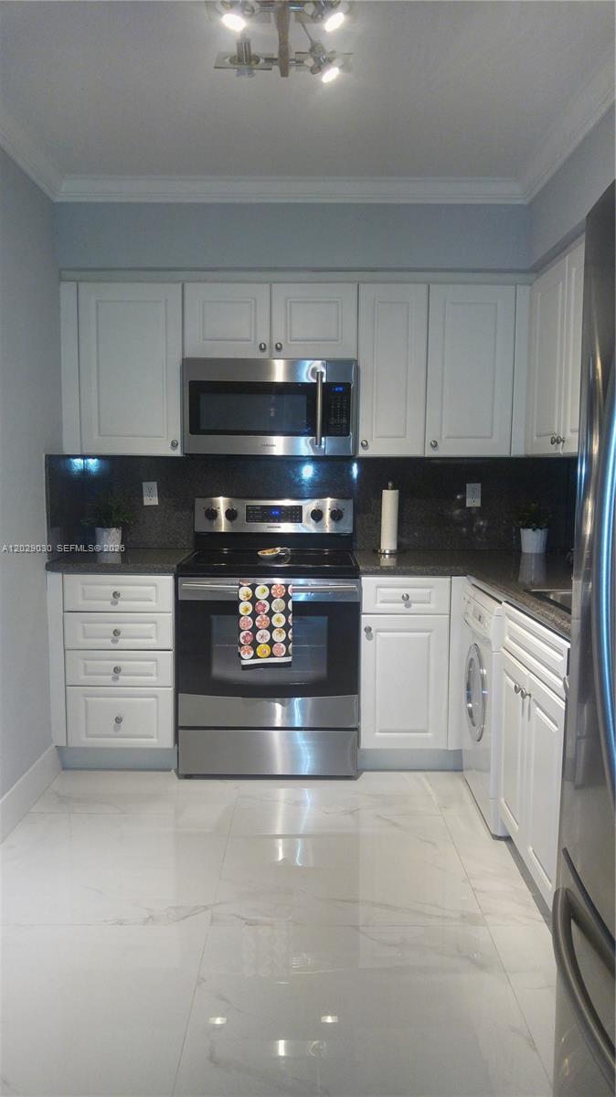 A kitchen features white cabinets, stainless steel appliances, dark countertops, and white marble-patterned flooring — 2501 S Ocean Dr # L04, Hollywood FL 33019, HOLLYWOOD, FL