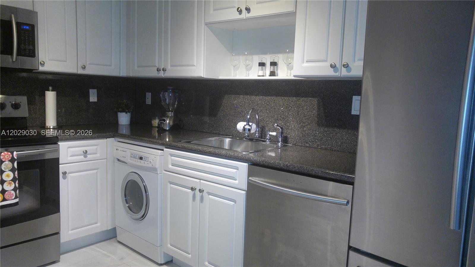 A kitchen features white cabinets, dark granite countertops, stainless steel appliances, and an integrated washer — 2501 S Ocean Dr # L04, Hollywood FL 33019, HOLLYWOOD, FL