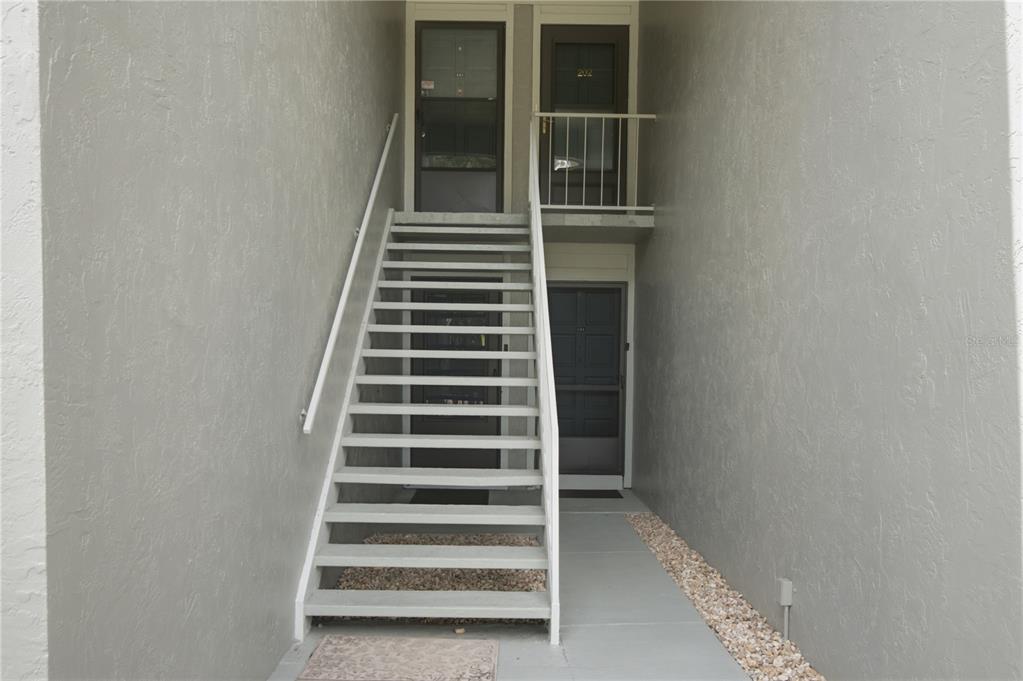 An exterior view shows a set of metal stairs leading to two second-floor apartment doors — 314 PALM COAST PARKWAY NE UNIT 202, PALM COAST, FL
